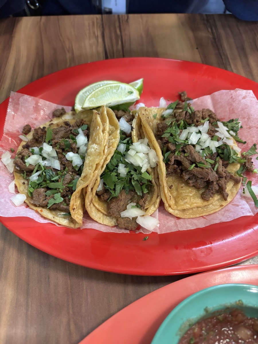 Street tacos on a red plate with cilantro, onion, lime, and fresh salsa